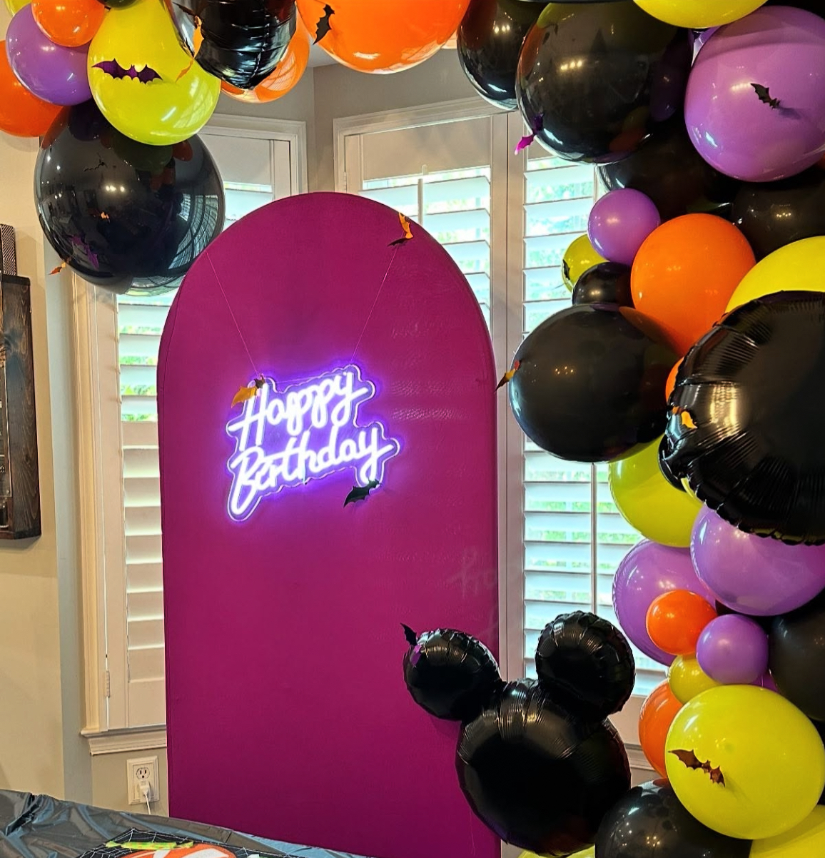 Halloween birthday backdrop with neon sign and bat balloon garland